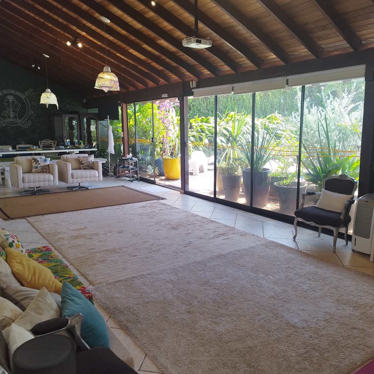 O salão da casa por dentro, com o jardim visto pelas paredes de vidro